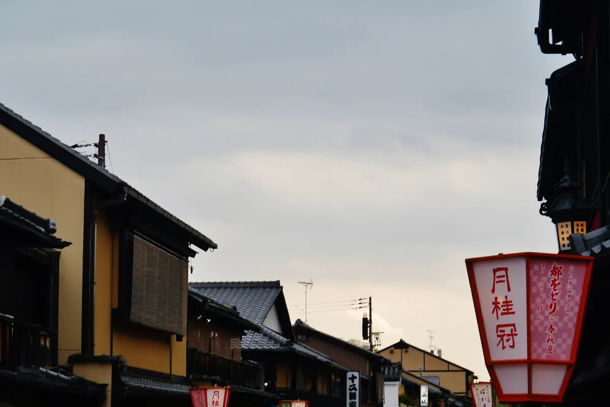 Red paper lanterns and dark wooden machiya houses along a street in Gion, Kyoto, under a dusk sky